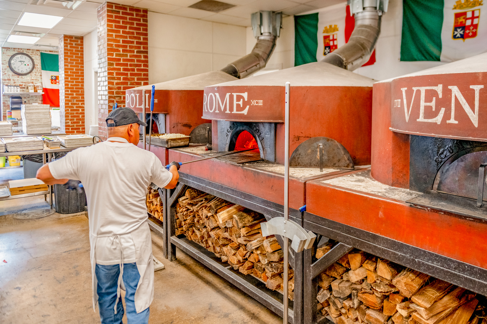 man putting pizza into red wood-fired pizza oven